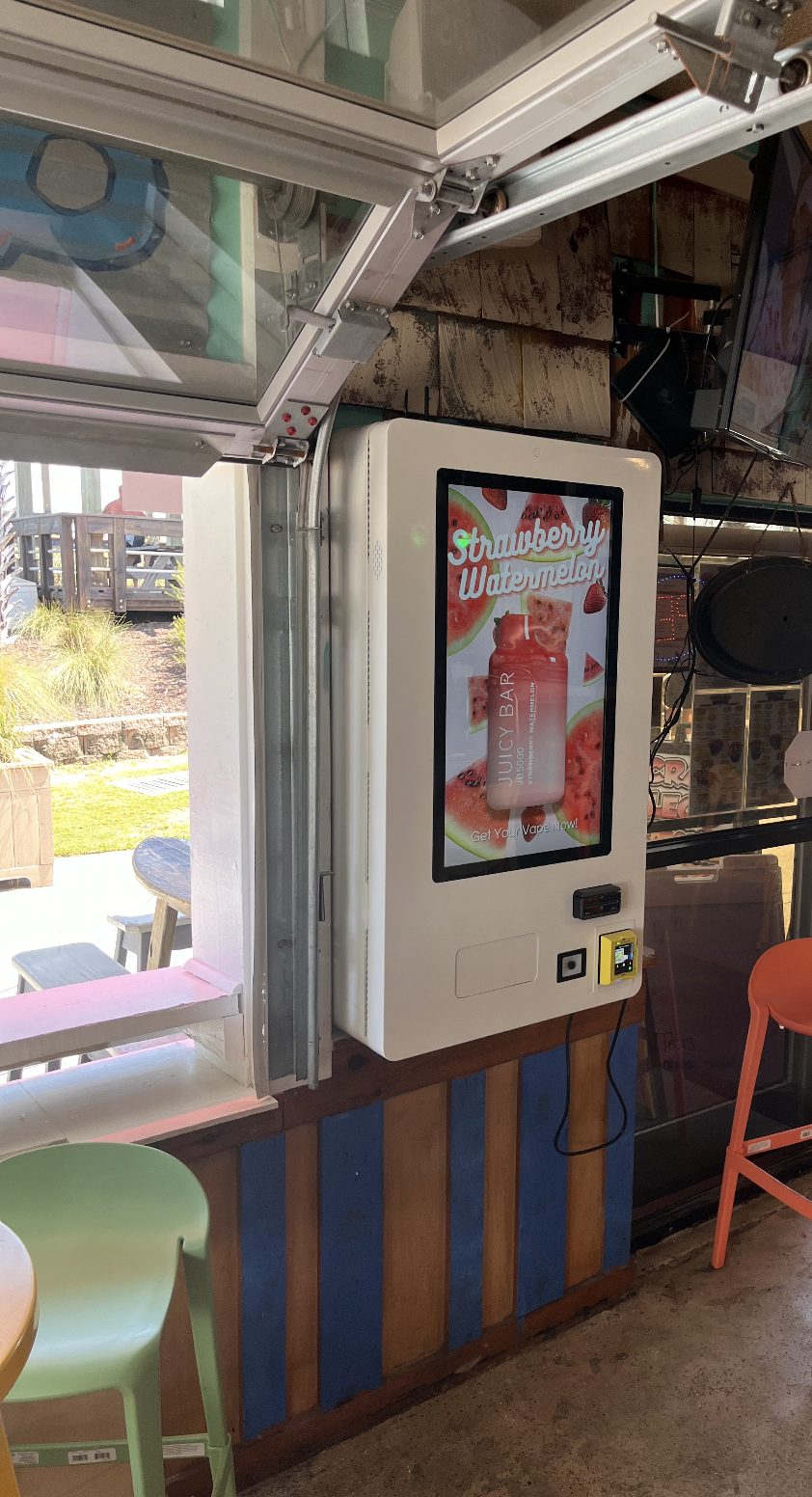 Fly Society vape vending machine on a bar's open-air patio, next to colorful bar stools