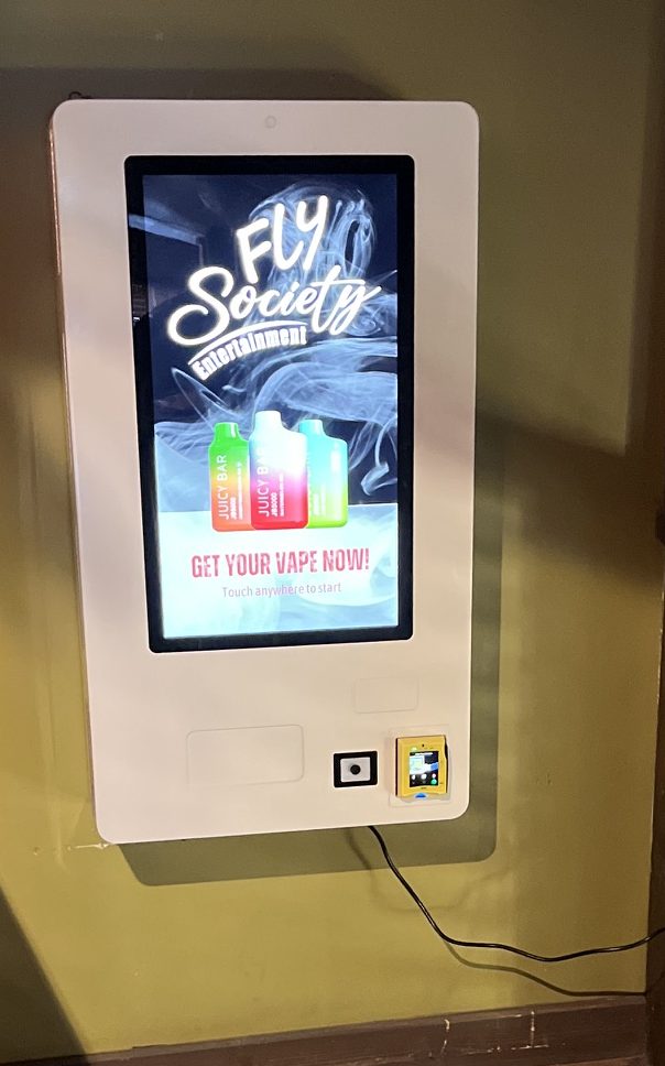 Wall-mounted Fly Society machine displaying the Fly Society logo and Get Your Vape Now on screen